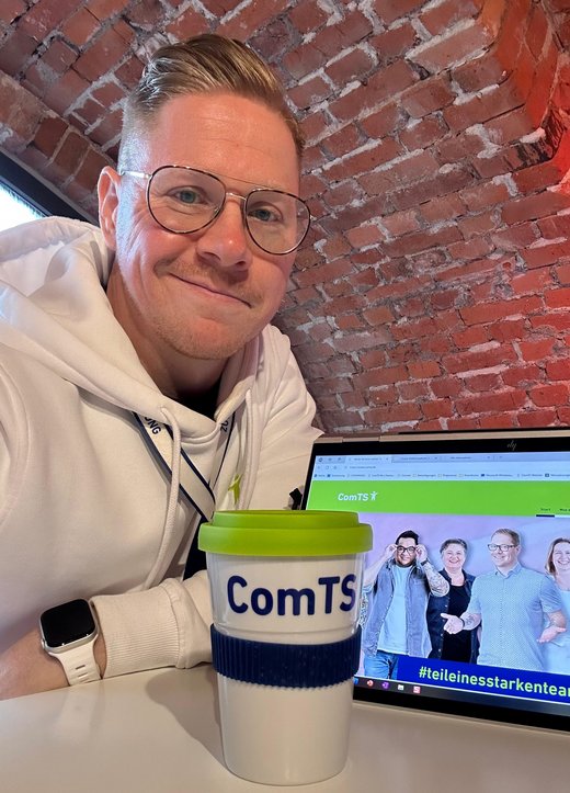 ein Mann schmunzelt mit ComTS Becher in die Kamera